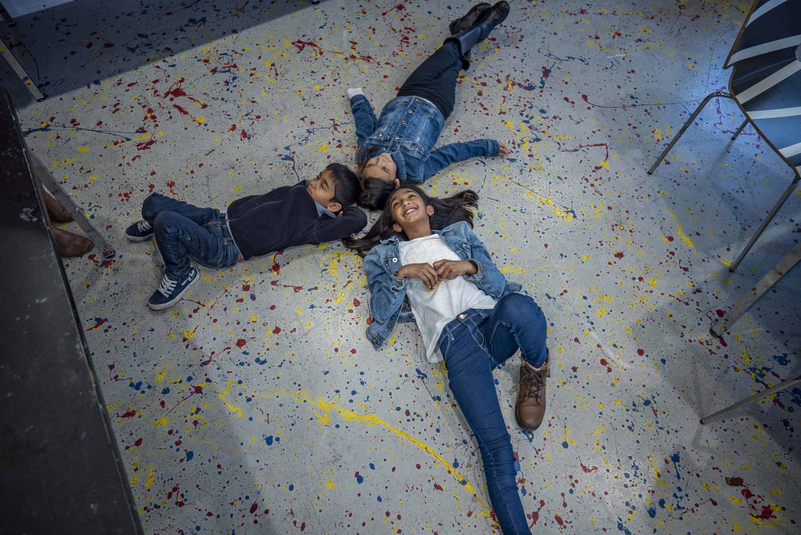 3 kids lying on painters cloth at Art Gallery of Burlington