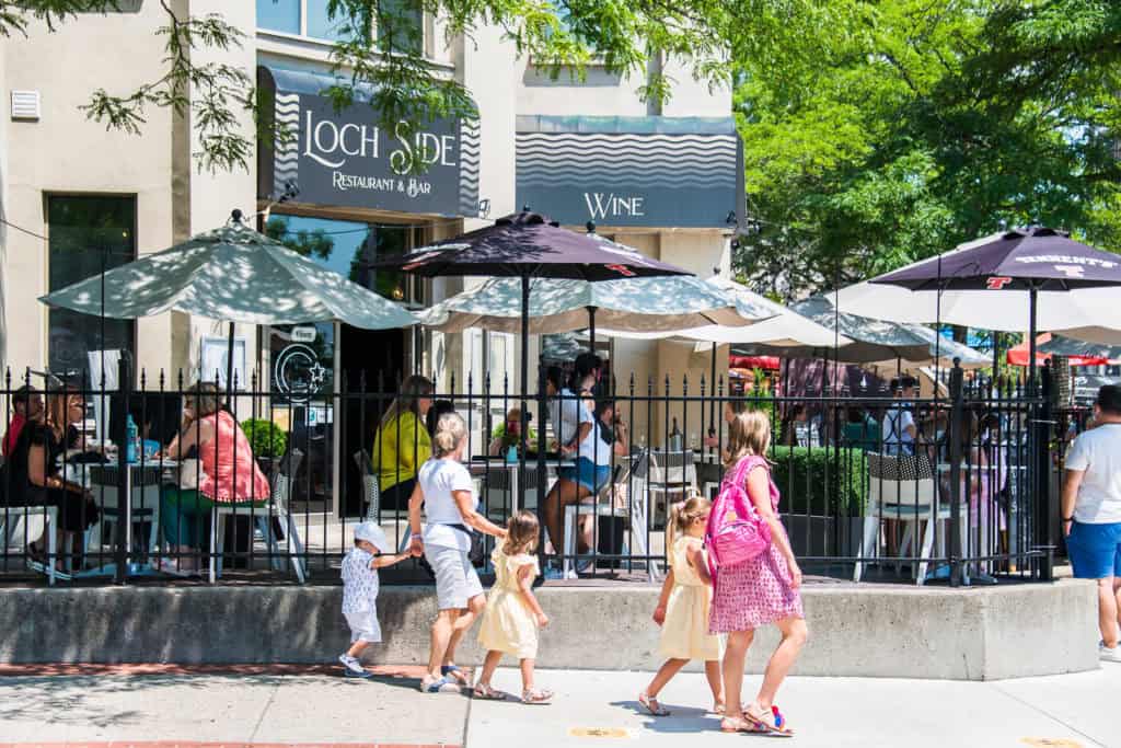 people walking on sidewalk past patio