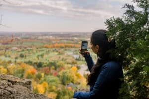 A young woman takes a picture overlooking Mount Nemo lookout with bright Autumn colours.